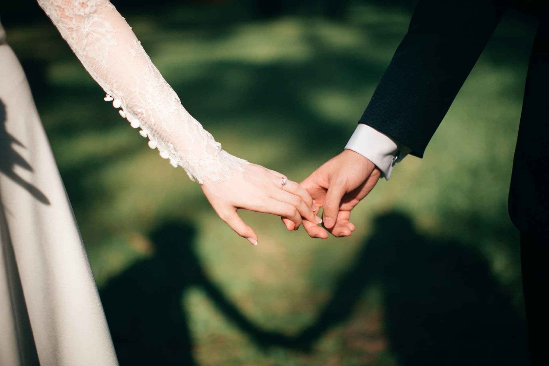 A bride and groom holding hands, their shadows falling across the grass.